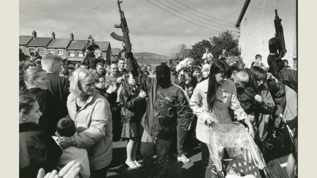 Black and white photograph of a crowd with men in balaclavas holding rifles