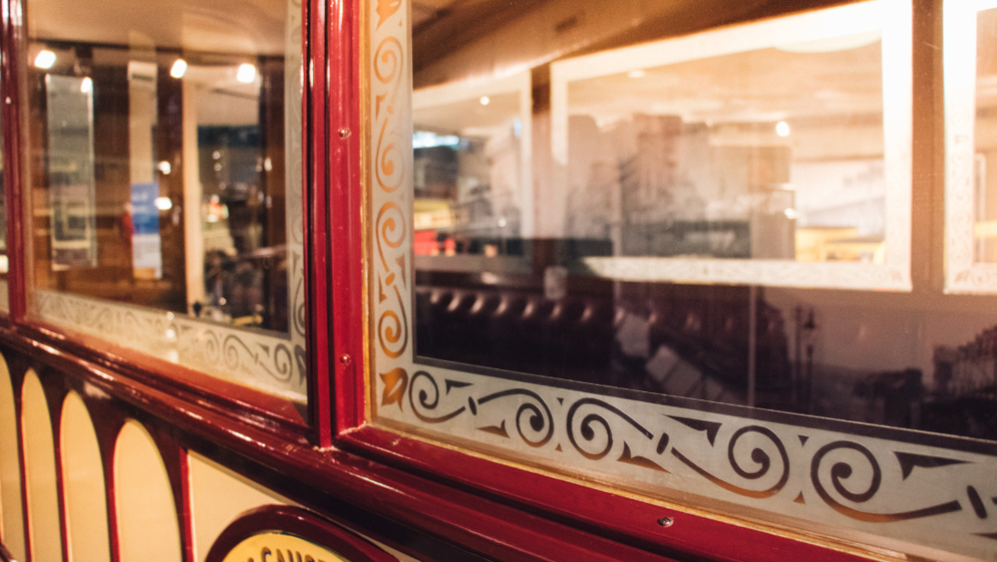 A view of the windows of a cream and red tram car. There is a frosted trim with swirly patterns.