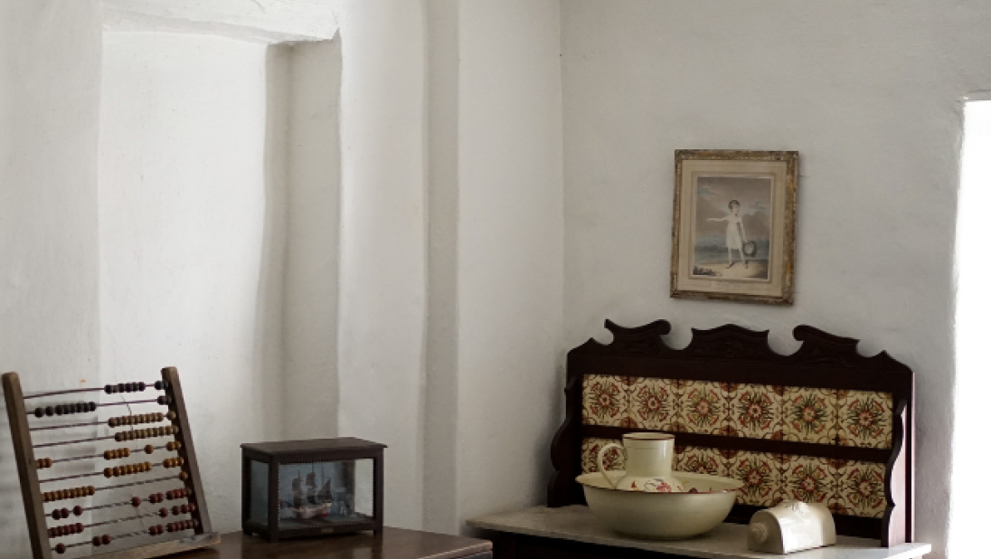 The interior of a cottage bedroom. A side table with a wash basin is visible. 