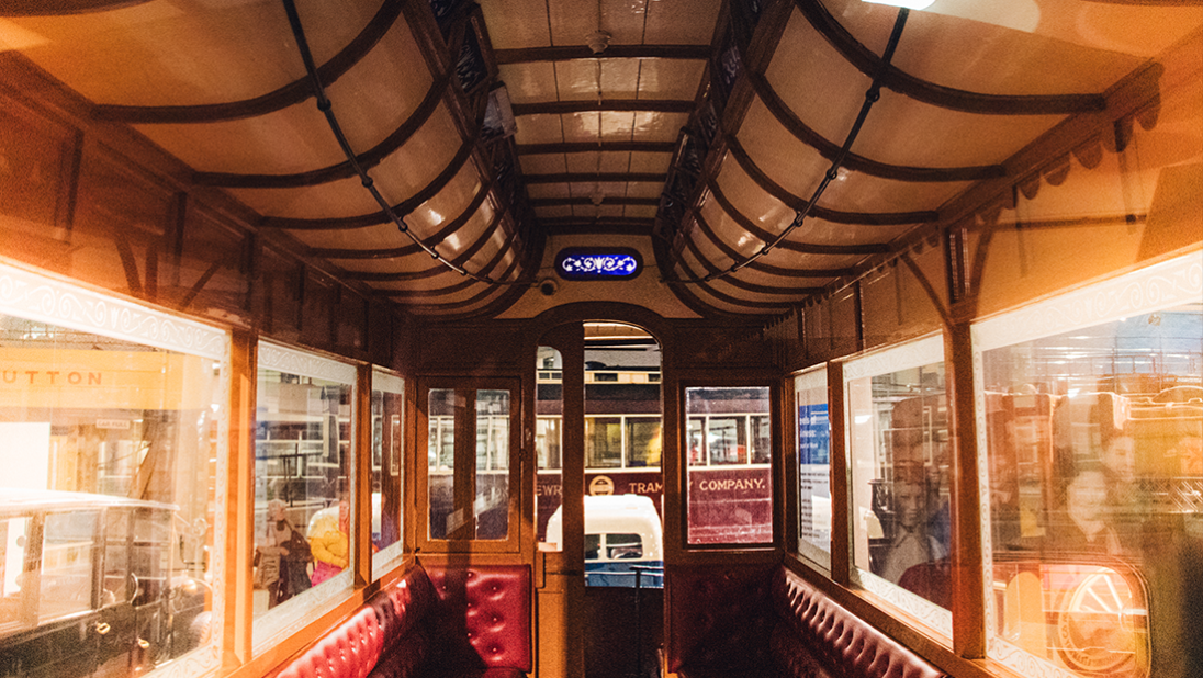 A view inside a cream and red tram car. There is a row of red leather seats on each side that exhude luxury.