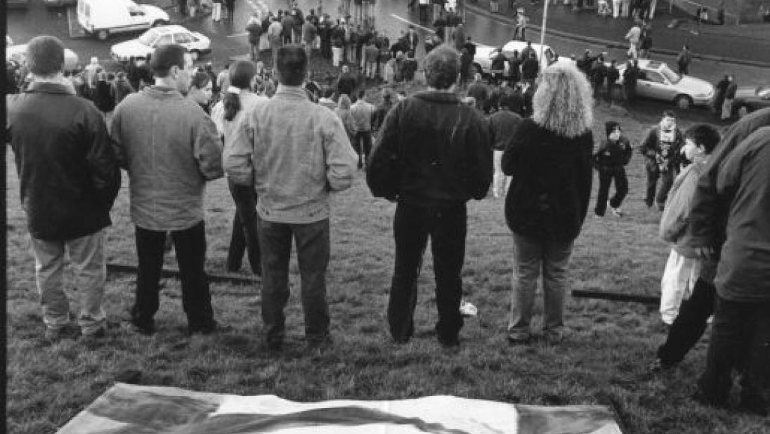 Black and white photograph of Bloody Sunday commemorations, large print of a person on a field, can see the back of crowds standing