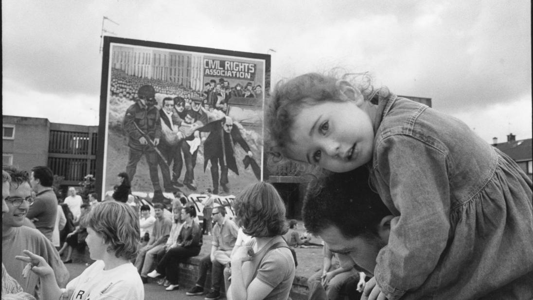 Black and white photograph of Bloody Sunday rally, young child on adults shoulders looking at the camera in the foreground