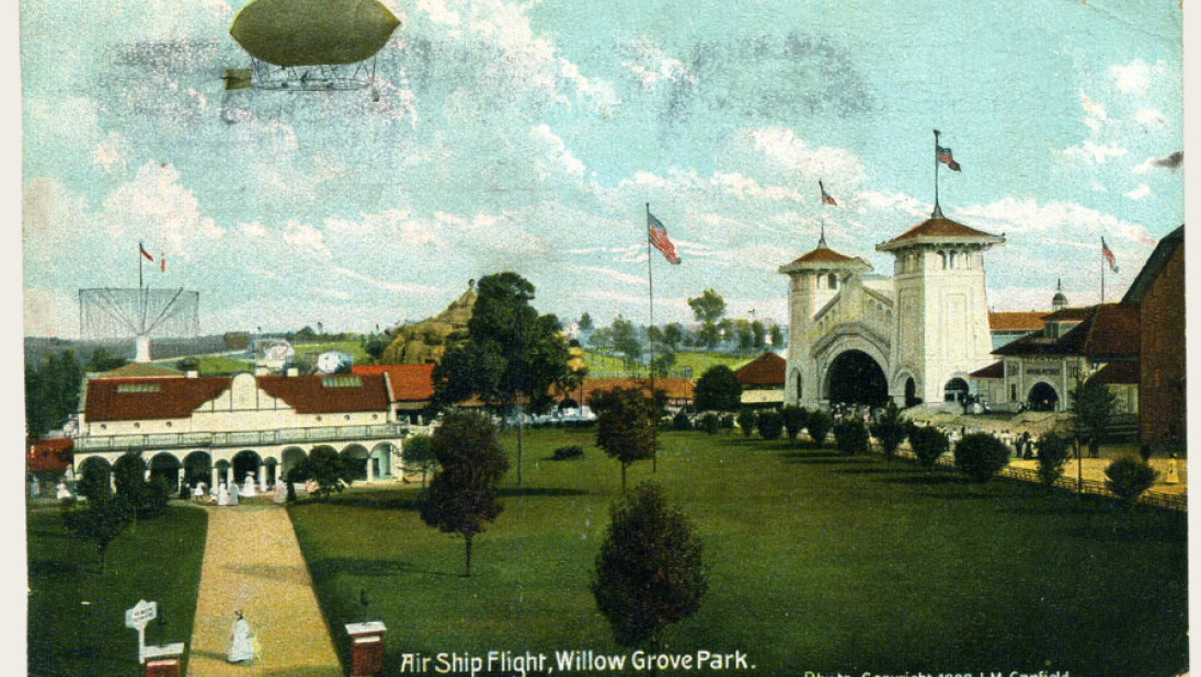 A postcard with a scene of a large park in America. An airship is in the sky.