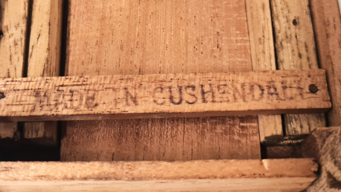 The underside of a table for a dolls' house. One of the beams is stamped 'MADE IN CUSHENDALL'