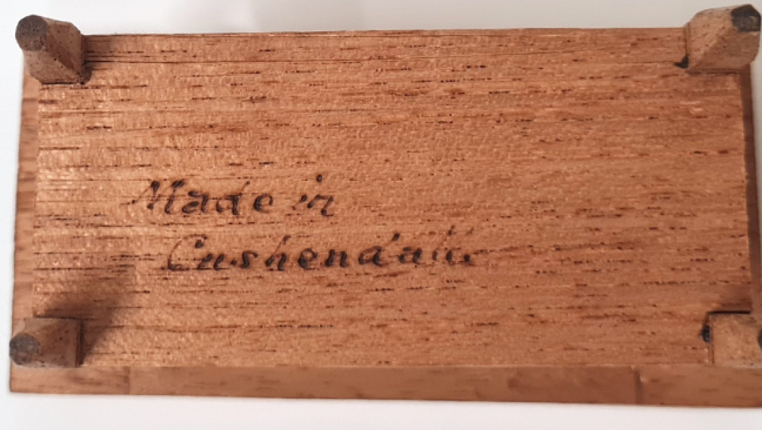 The underside of a wooden table for a basin, for a dolls' house. The words 'Made in Cushendall' are written in cursive. 