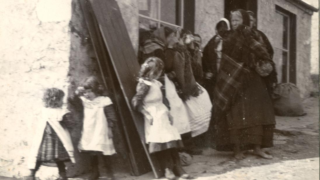 A woman and children stand outside their cottage wearing traditional dress in the early 1900s.