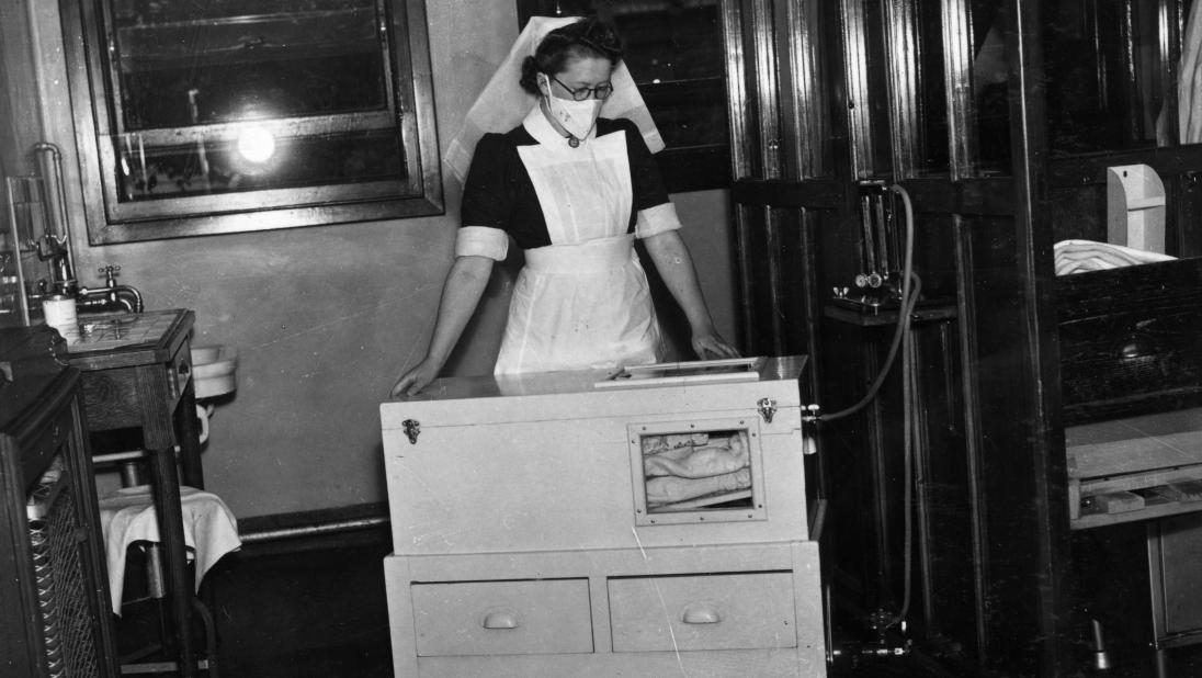 A nurse stands over an electrically-heated cot.