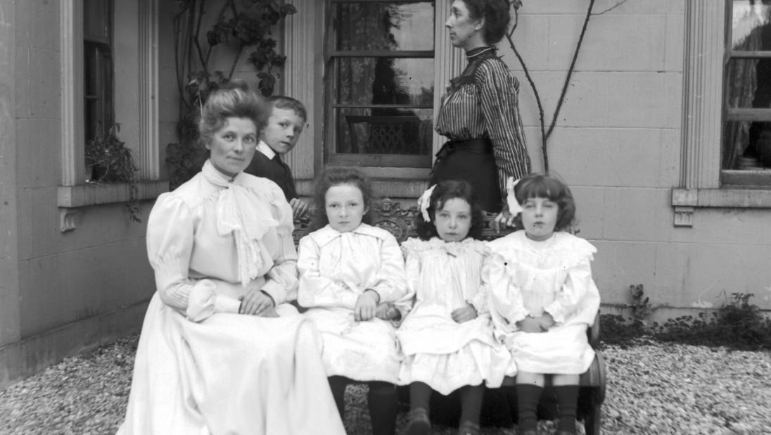 Two women sit with three children looking very well to do in the early 1900s. 