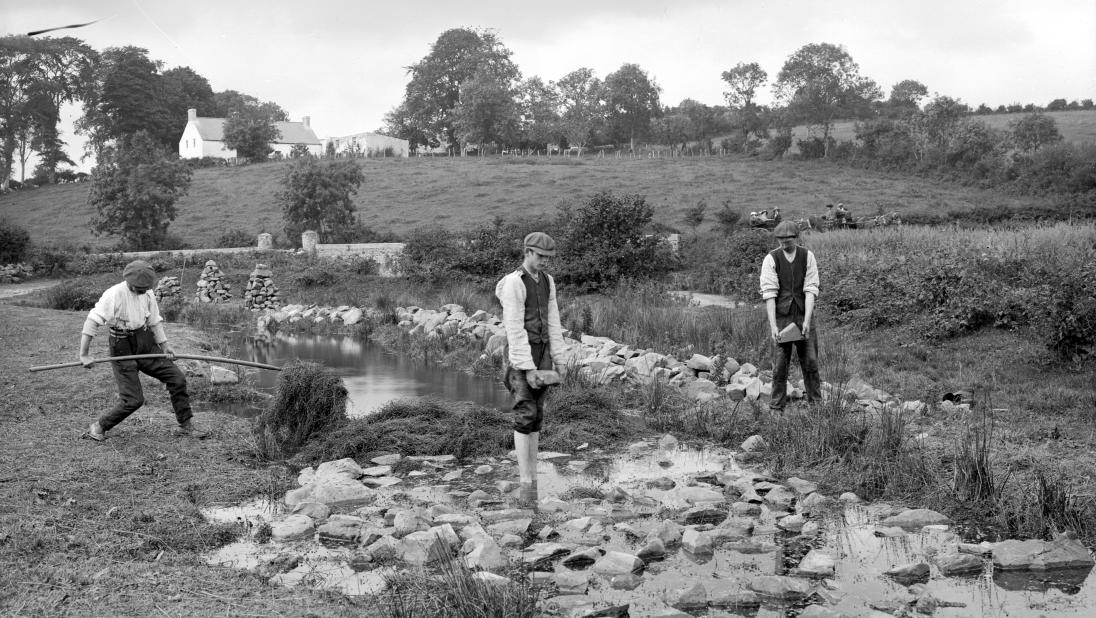 Men weigh the flax down with stones in the dam