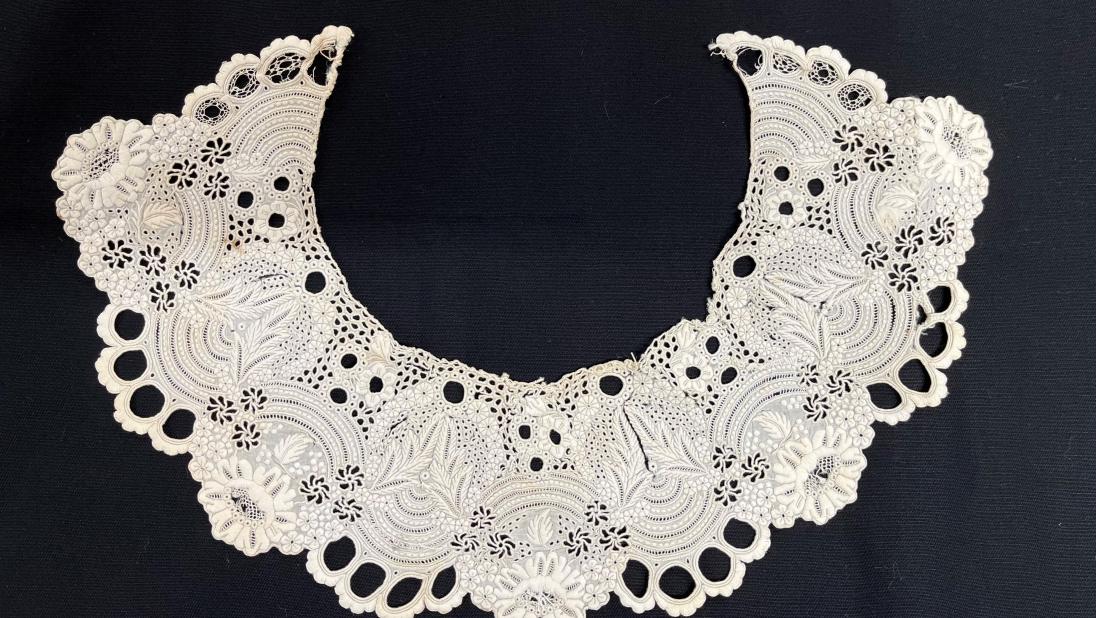 Detail of embroidery on a white dress collar from c.1860. It is placed on a black background