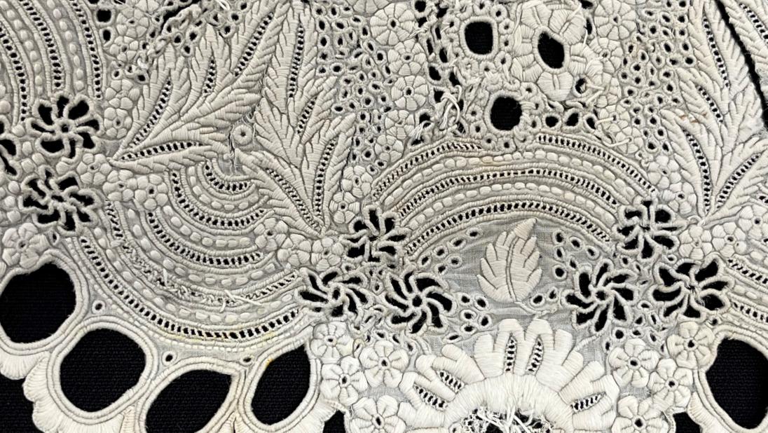 Detail of embroidery on a white dress collar from c.1860.  It is placed on a black background