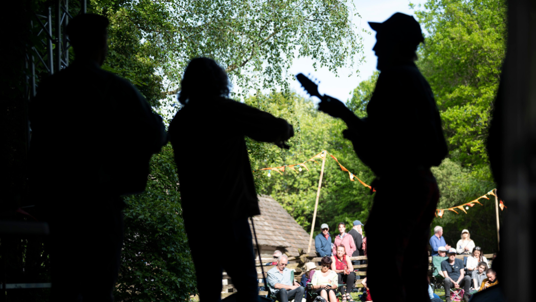 The silhouettes of three musicians on a stage playing, with sights of the crowd in the background.