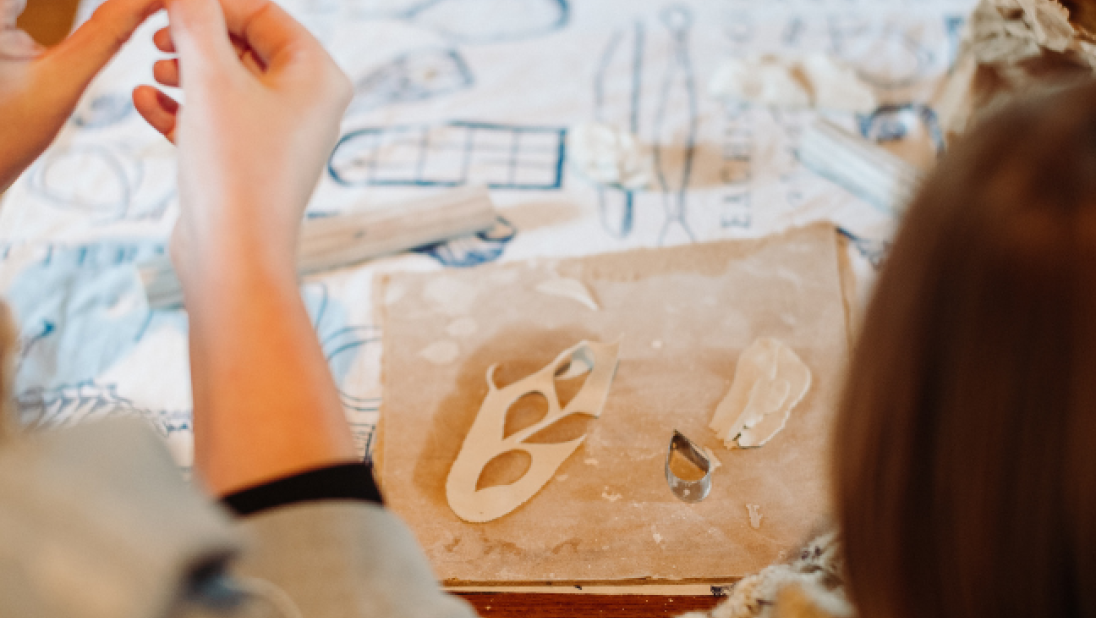 a womans hands doing crafts and a child sitting next to her