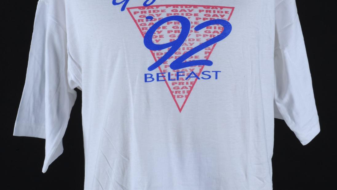 A white tshirt made for the second pride in Belfast. The logo is an inverted pink triangle with ''92' written in it.