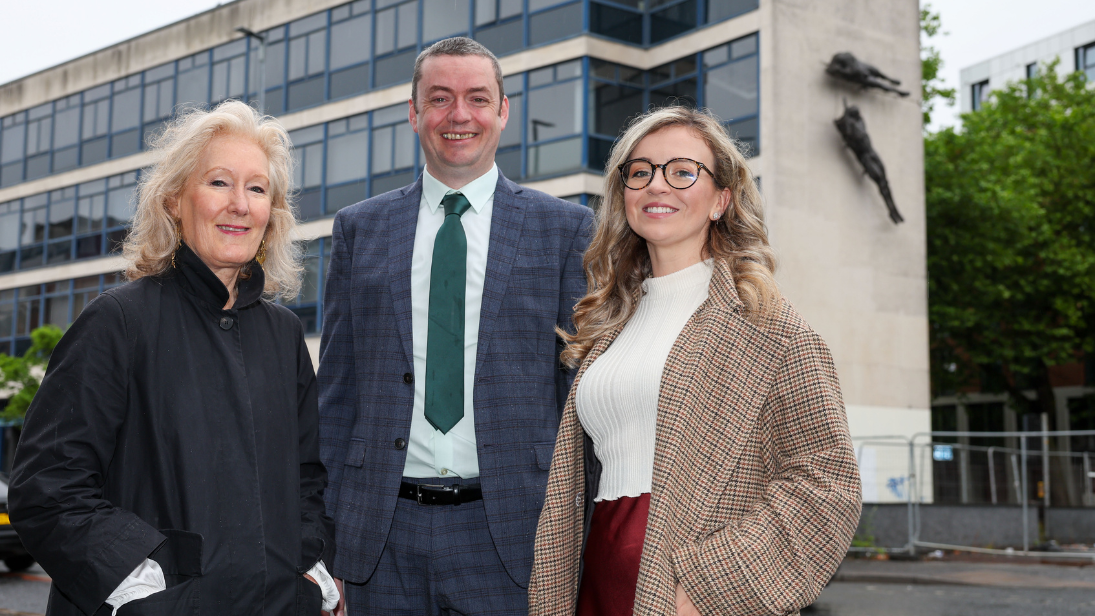 Three people smartly dressed standing in front of the old Ulster Bank building in Shaftesbury Square in Belfast, showing two aluminium Elisabeth Frink sculptures on the wall