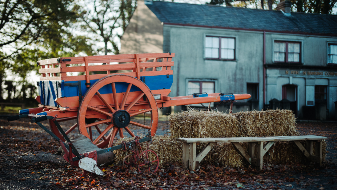 Hay bales and a bench, with an orange and blue cart sitting