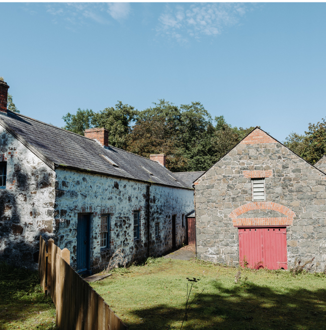 Two stone buildings sit in a sunny field.