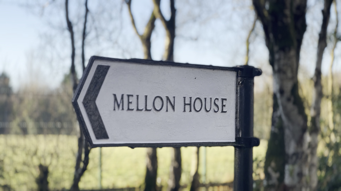 A white sign in a countryside setting, that reads: 'Mellon House'.