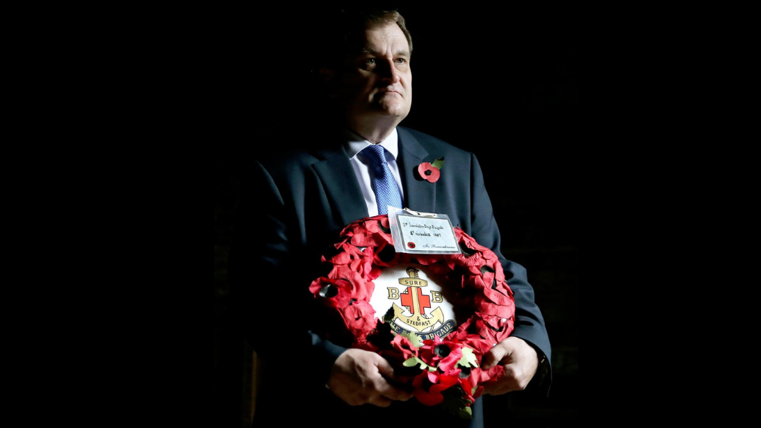 Man in a suit holding a poppy wreath with black background