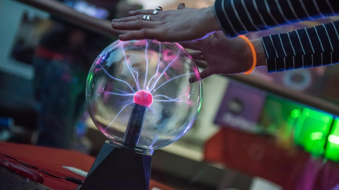 A set of hands on a plastic ball which is giving off sparks of purple energy