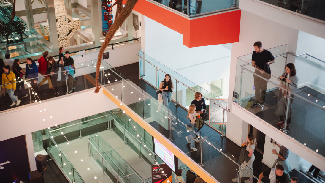 People walking around floor levels of the Ulster Museum. Festoon lighting in the foreground.