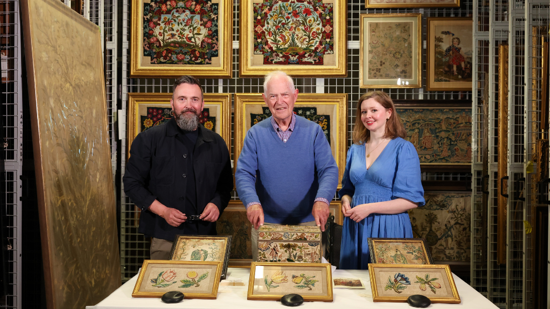 Three people standing behind a display of needlework