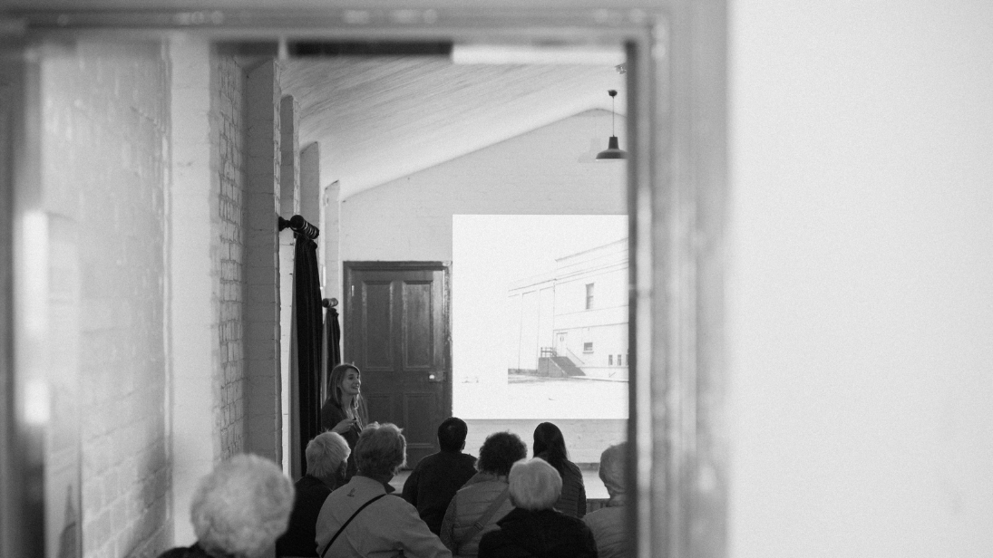 A black and white image of backs of heads and a lady giving a lecture