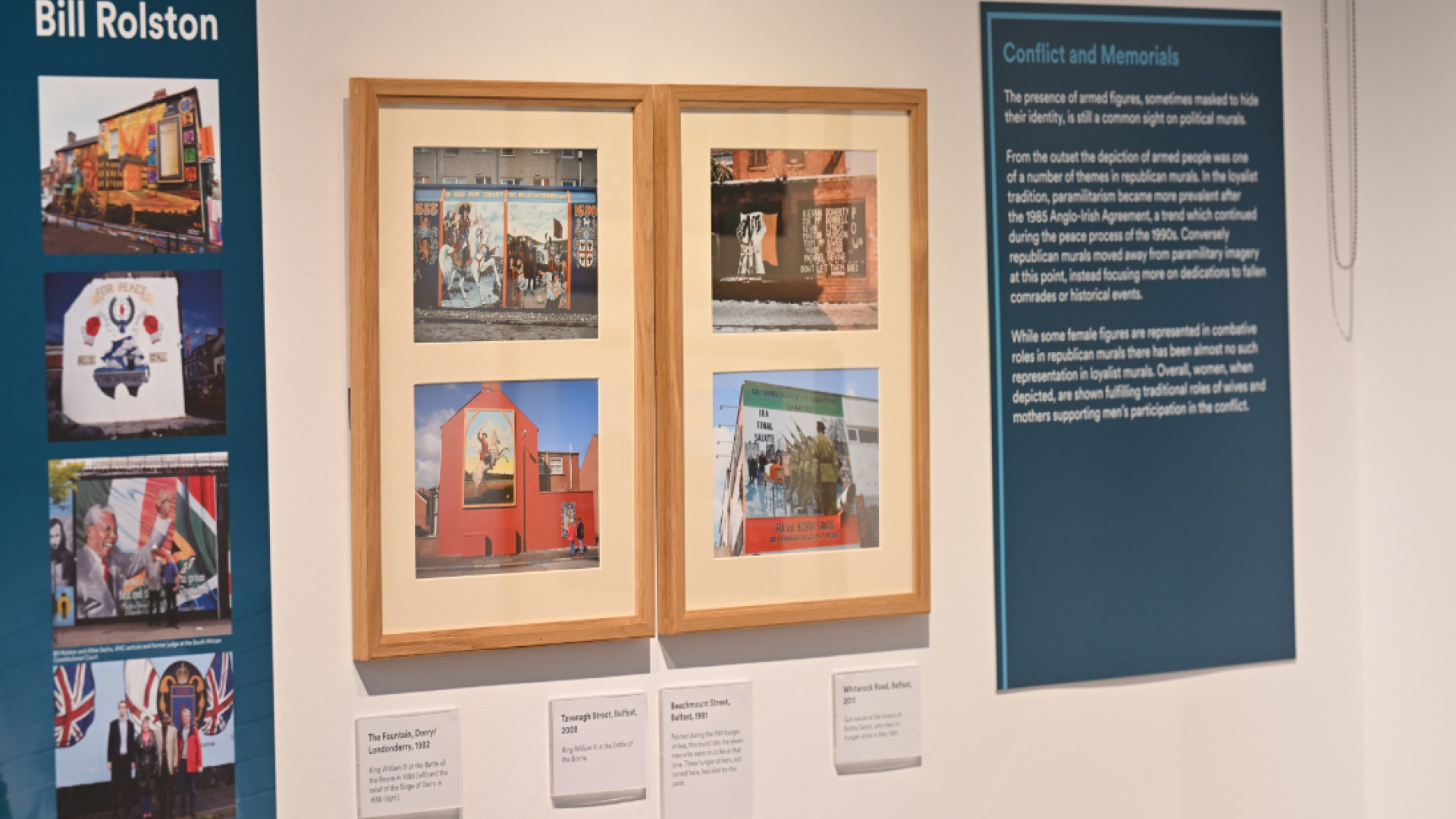 Four photographs of murals in wooden frames hung on a white wall inside a room in the Ulster Museum. Two turquoise coloured text panels are positioned on either side of the frames.
