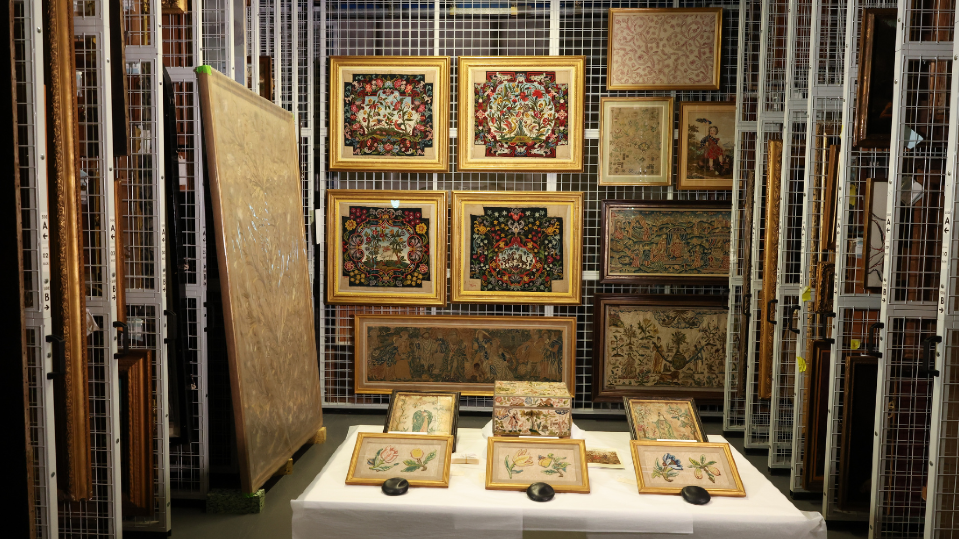 A display of needlework both on a table with a white table cloth and on wire racking to the back and sides of the photo area.