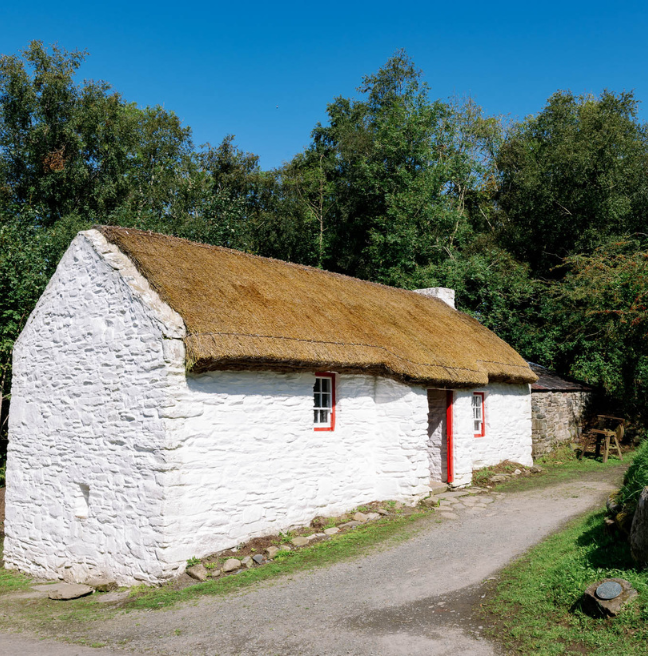 A whitewashed thatched cottage sits in the sunlight.