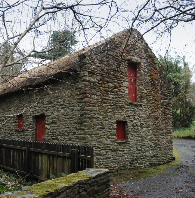 A stone building with red windows and doors and a thatched roof.