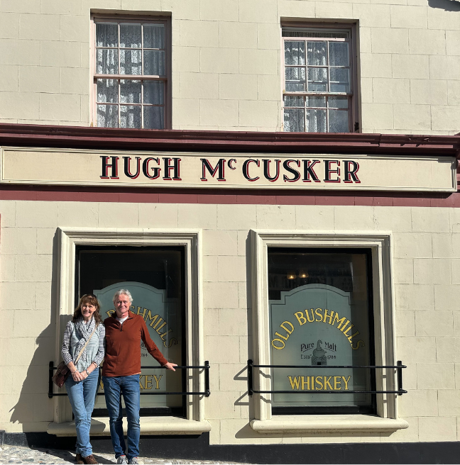 A man and a woman stand outside a pub. The name Hugh McCusker is written above the windows.
