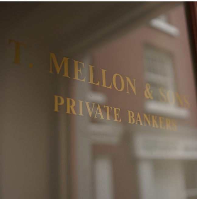 The glass door to a bank, etched with the words 'T Mellon & Sons, Private Bankers'