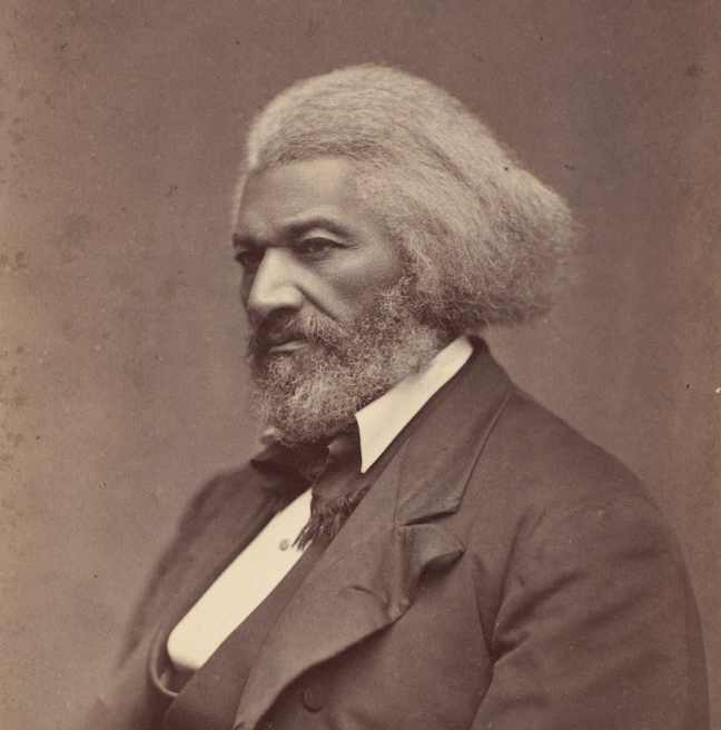 A man sits for a photograph in the late 1800s. He looks strong and stoic, facing away from the camera. 