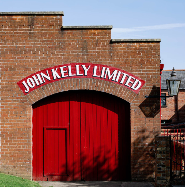 A red-brick facade with a red door, painted sign reads: John Kelly Limited