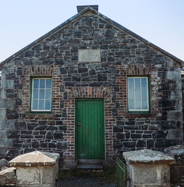 A stone school with a green door stands in the sunshine