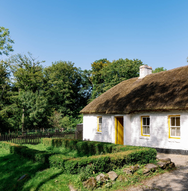 A thatched white cottage with yellow doors and windows and a large garden. 