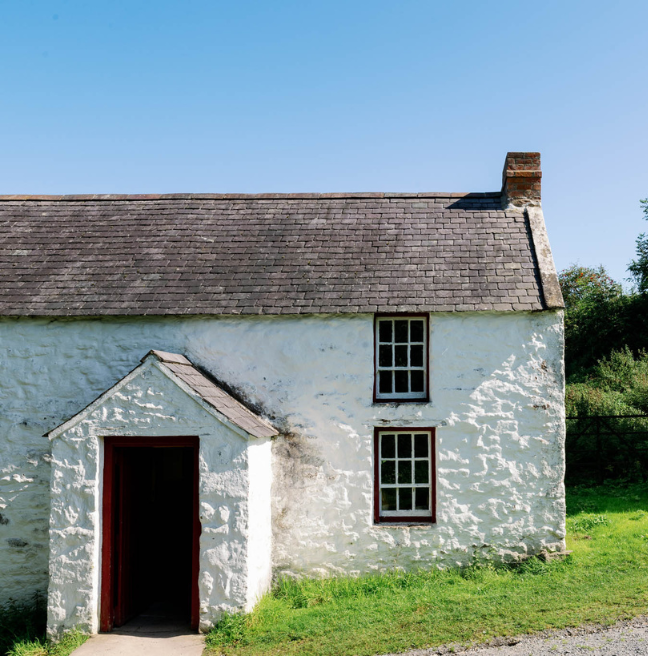 A white house with a slate roof, on a sunny hill.