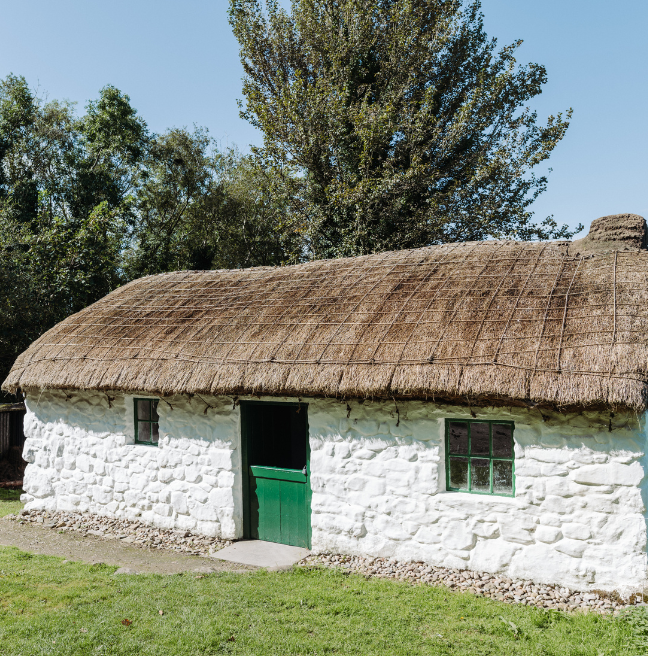 A whitewashed cottage with a thatch roof and green trims.