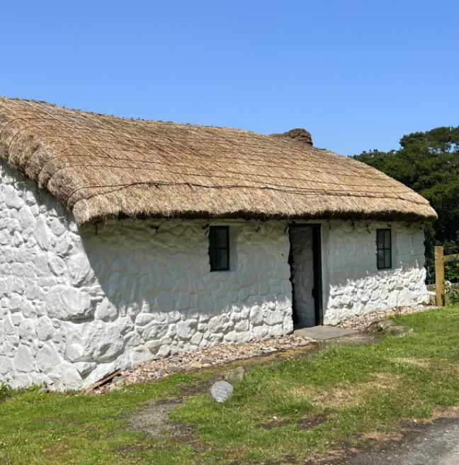 A whitewashed cottage with a thatch roof on a sunny day.