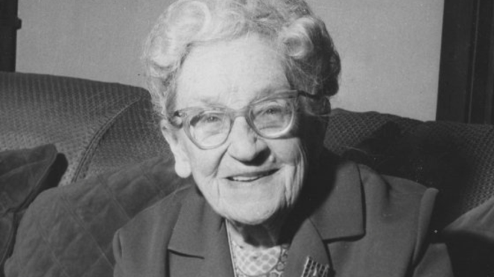 A smiling older woman looks at the camera in a black and white photograph.