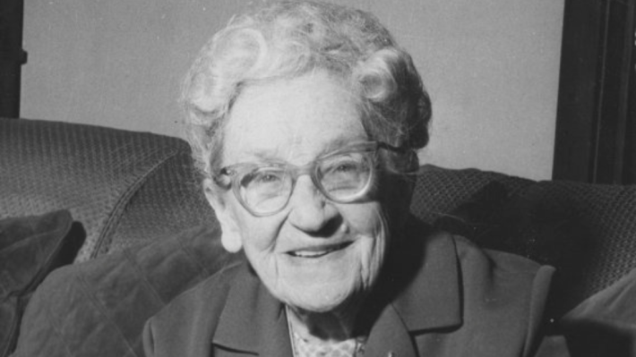 A smiling older woman looks at the camera in a black and white photograph.