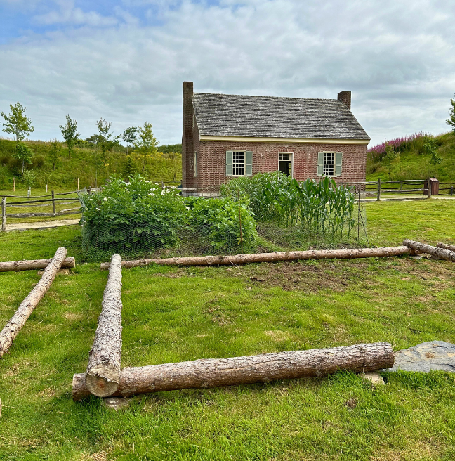 Image of a red brick house with a garden and cabin outline in the foreground