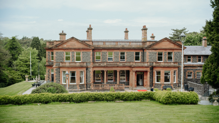 The grand historic Cultra Manor building at the Ulster Folk Museum, surrounded by manicured lawns under a clear sky, near Holywood, Northern Ireland.