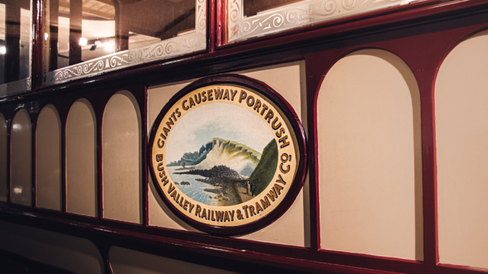 The side of an old tram with a logo reading 'Giants Causeway Portrush Bush Valley Railway & Tramway Co'. 