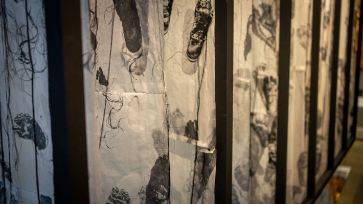 Image of installation in the window on our world gallery with black ink footprints on suspended fabric between black beams