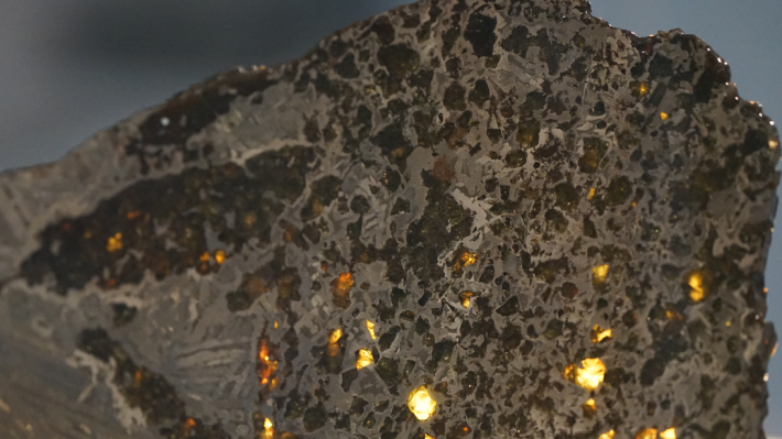 A close-up of a meteorite. The surface is rough and pocketed, with flashes of light through it.