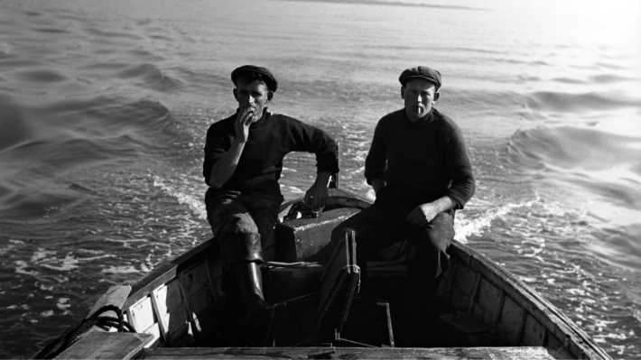 A black and white image of two men sitting on a fishing boat