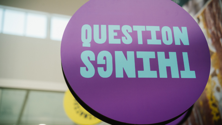 A purple sign which says question things