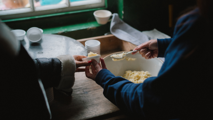A lady buttering a piece of bread and handing it to another lady. 